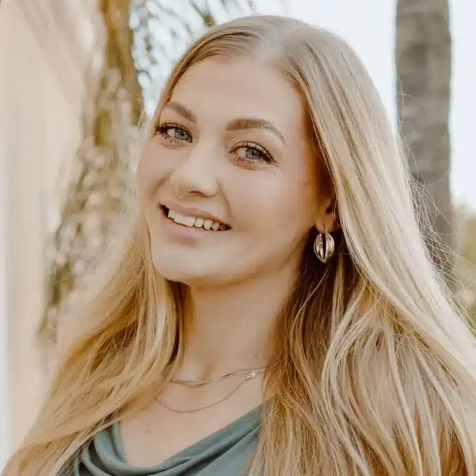 Smiling young woman with long blonde hair outdoors in natural light.