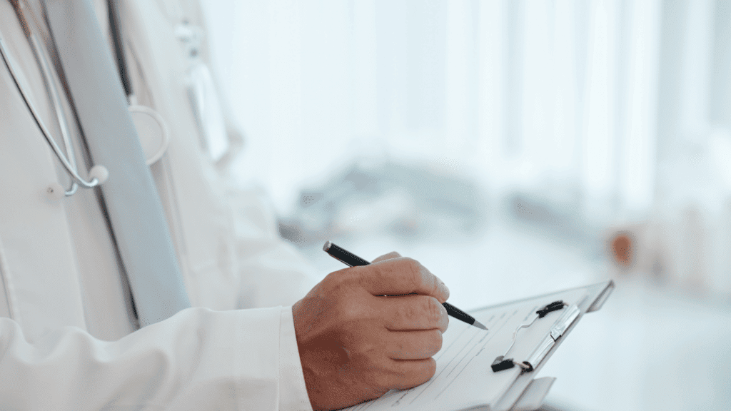 Doctor reviewing patient records and writing notes in a clinical setting.